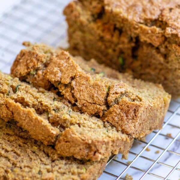 A loaf of zucchini bread with three slices cut out laying on a wire rack.
