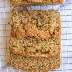 A loaf of zucchini bread with three slices cut off and laying on top of each other on a wire rack.