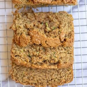A loaf of zucchini bread with three slices cut off and laying on top of each other on a wire rack.
