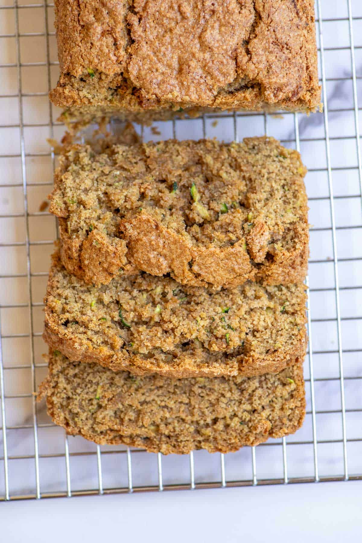 A loaf of zucchini bread with three slices cut off and laying on top of each other on a wire rack.