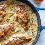 A large cast iron skillet on a countertop filled with chicken breasts sitting in a cream sauce with sliced peaches.