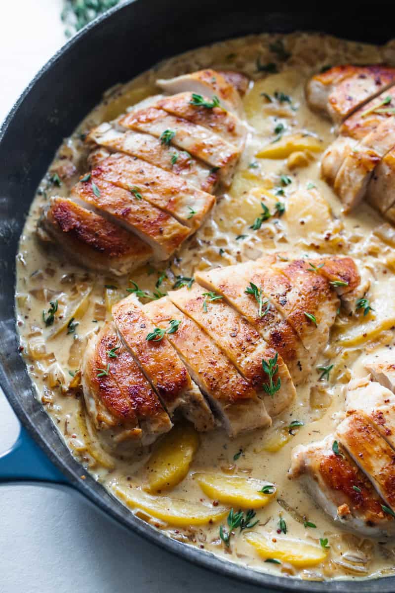 Chicken breasts in a cream sauce with peaches in a cast iron skillet.