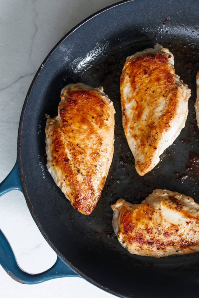 Chicken breasts seared in a large cast iron skillet.