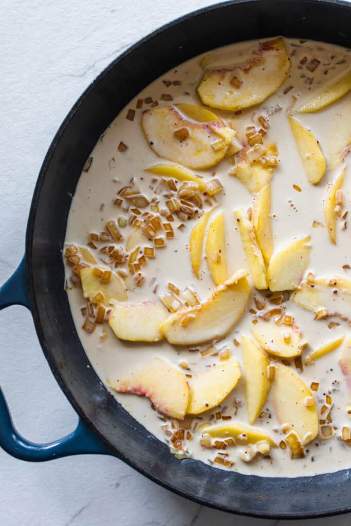 A cream sauce with peaches and cooked onion in a large cast iron skillet.