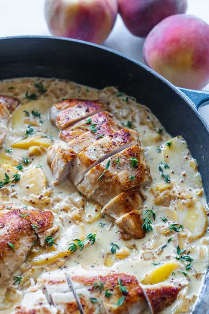 Chicken breasts sliced and placed in a cast iron skillet full of cream sauce with peaches and seasonings.