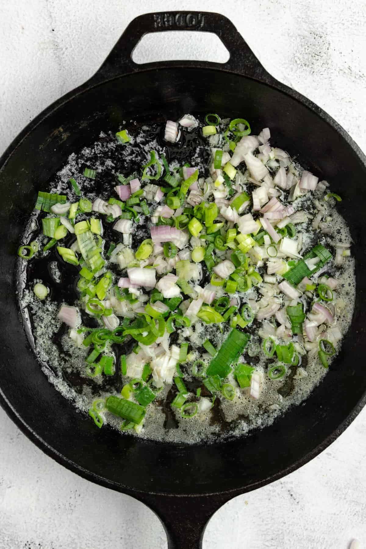 shallot, green onions and zucchini sautéing in a cast iron skillet.