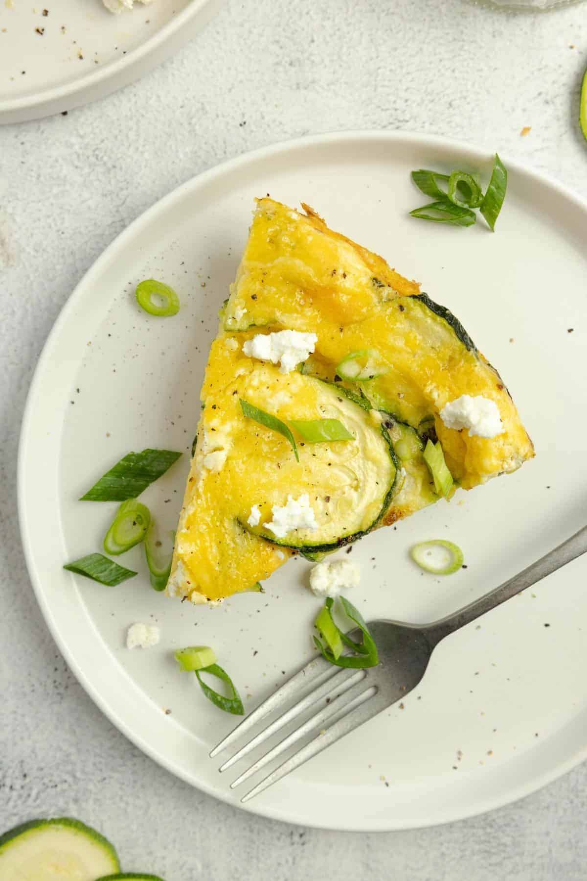 Slice of zucchini frittata topped with herbs on a white plate.