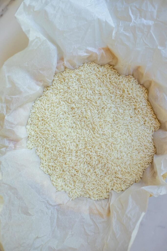 A crust in a pie pan covered in parchment paper and filled with rice.