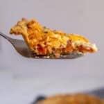 A pie scoop with a piece of tomato pie on it being lifted out of a pie in the background.