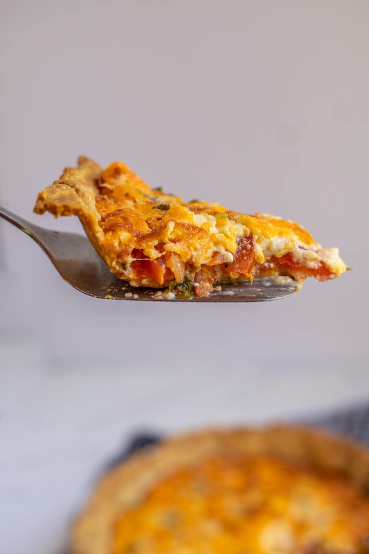 A pie scoop with a piece of tomato pie on it being lifted out of a pie in the background.