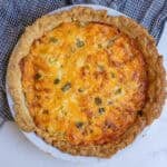 A tomato pie baked to a golden brown in a pie plate sitting on a countertop.