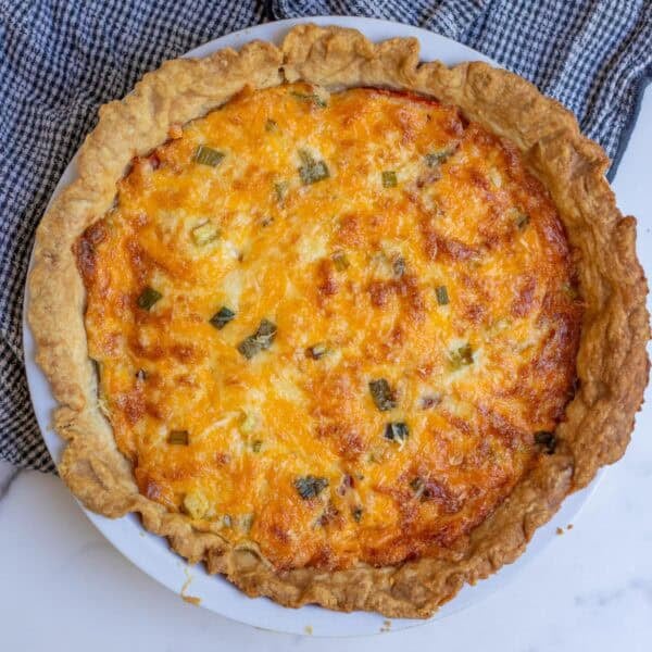 A tomato pie baked to a golden brown in a pie plate sitting on a countertop.