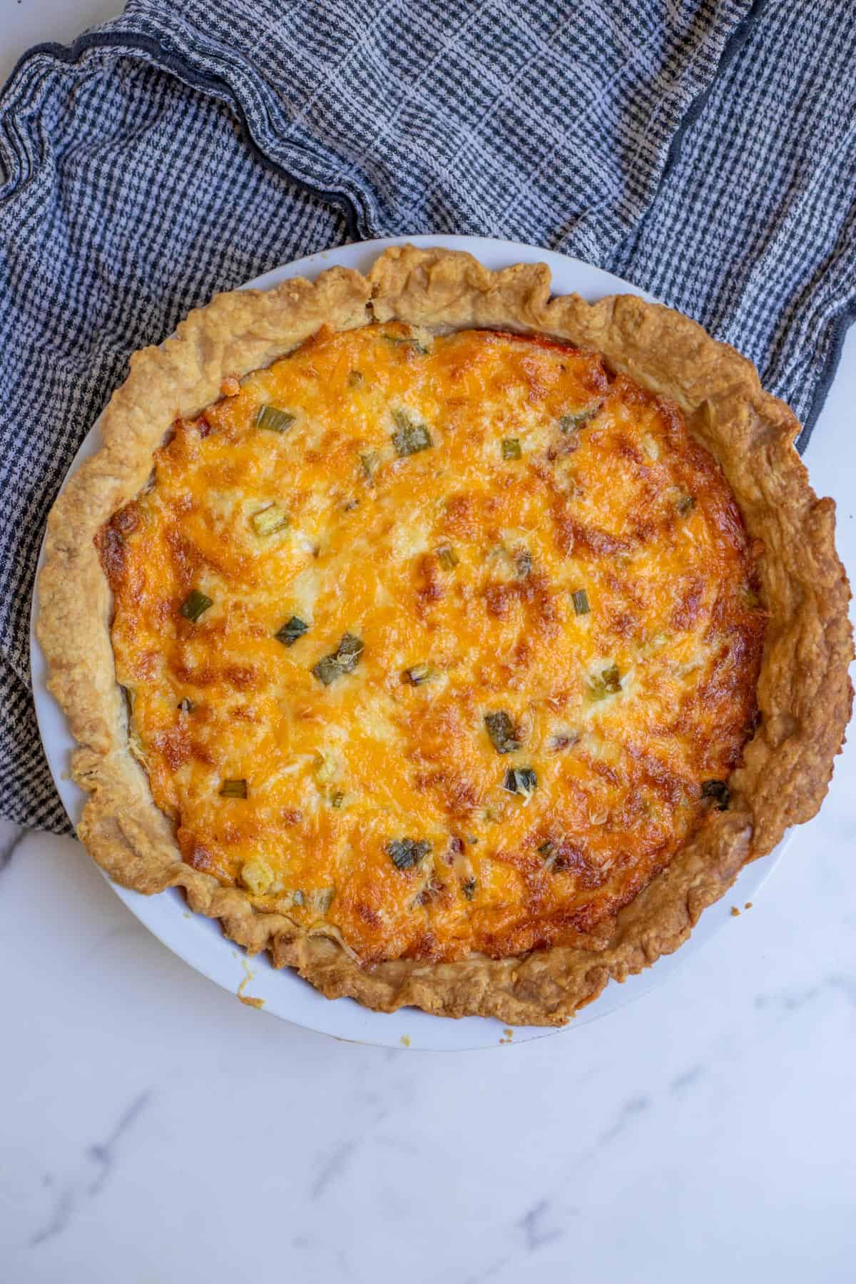 A tomato pie baked to a golden brown in a pie plate sitting on a countertop.