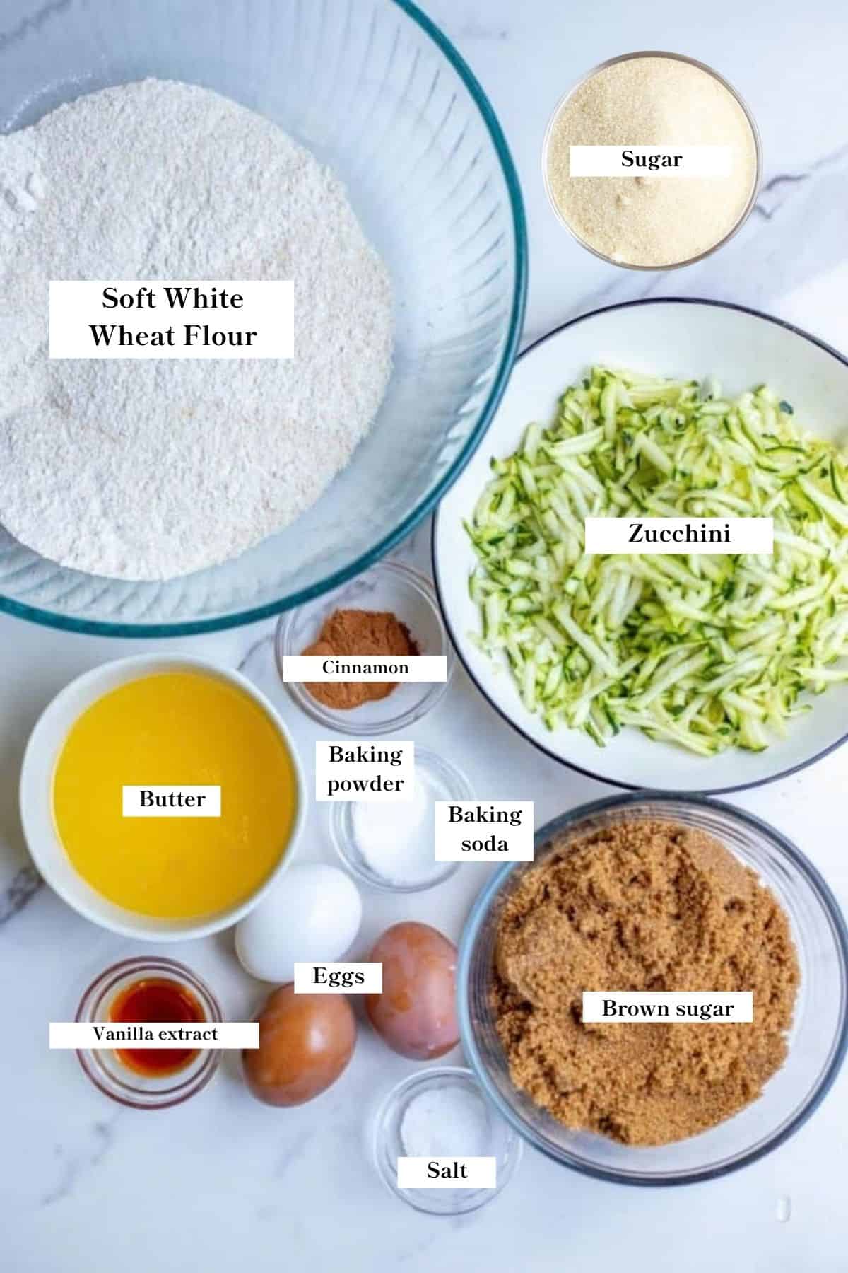 Ingredients for whole wheat zucchini bread in bowls on a white counter top.