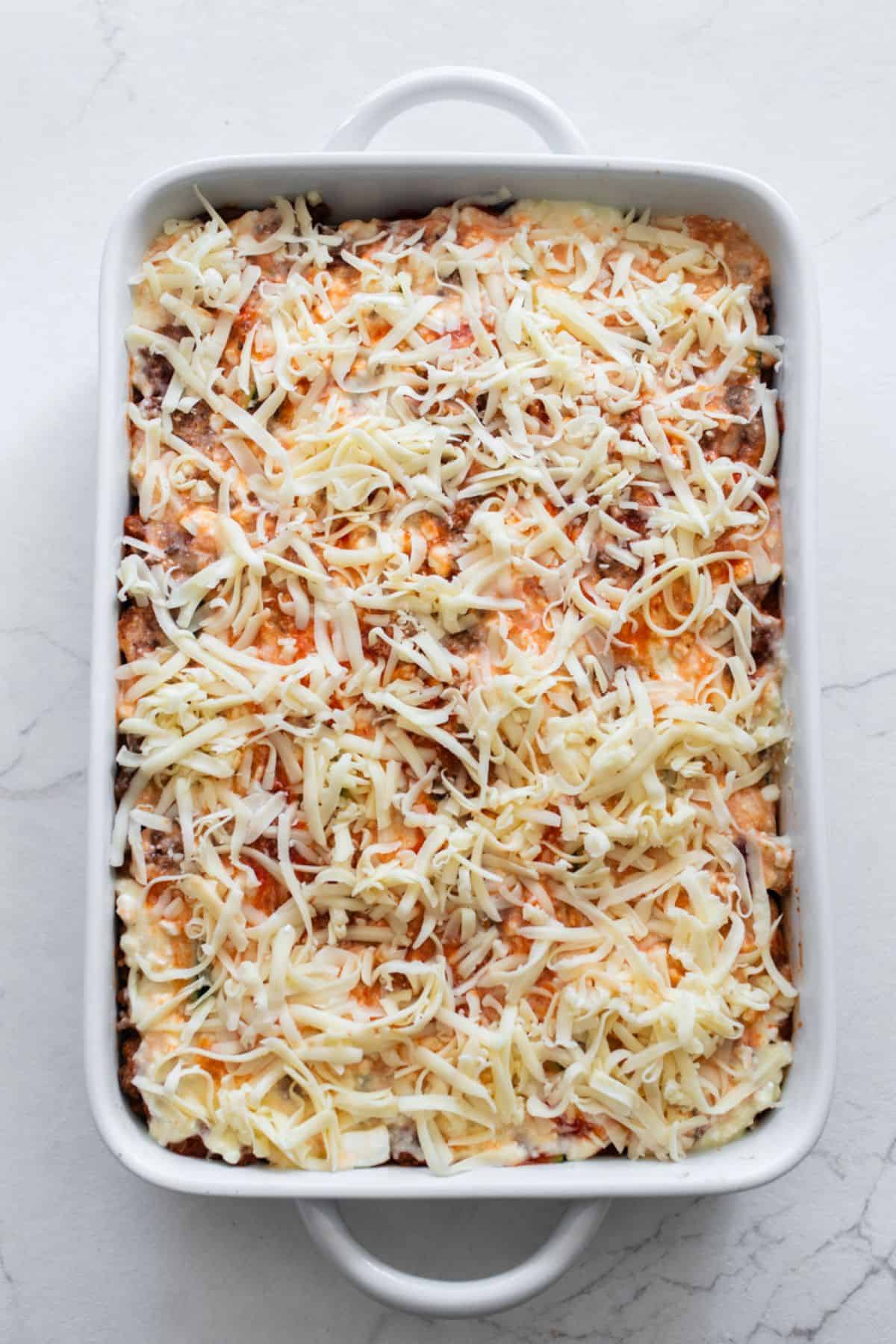 A filled casserole dish of meat sauce and zucchini slices, topped with shredded cheese.
