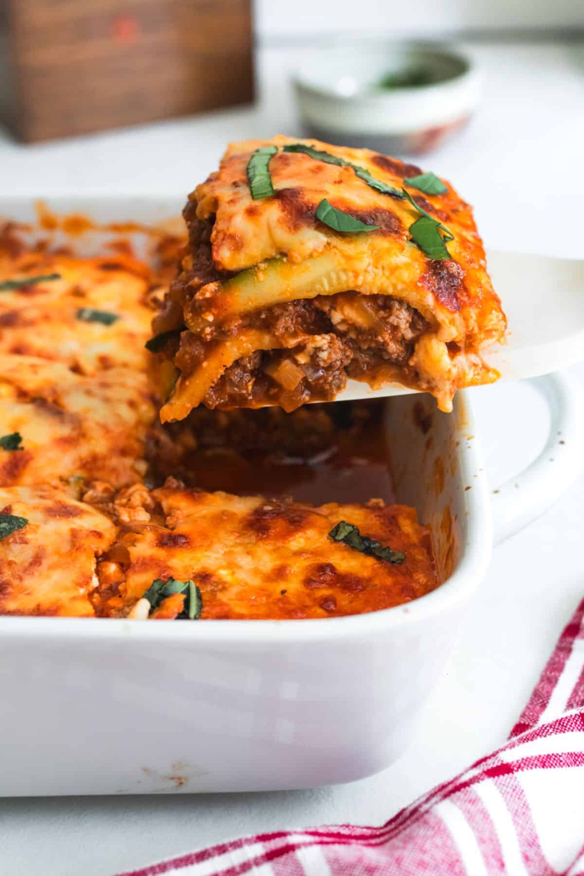 A slice of zucchini lasagna being lifted out of a casserole dish.