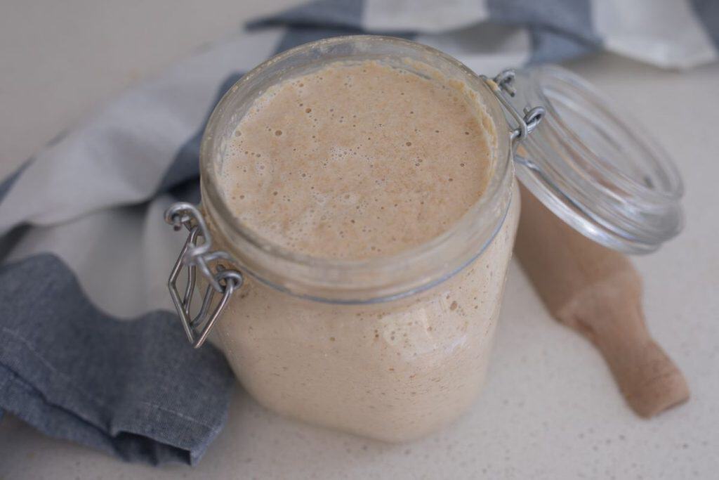 A lock top jar full of active sourdough starter with the lid open.
