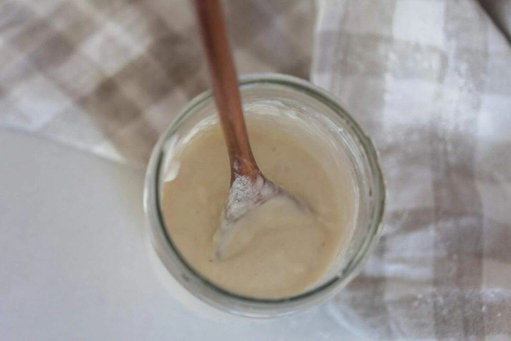 A jar of sourdough starter with a wooden spoon scooping some out.