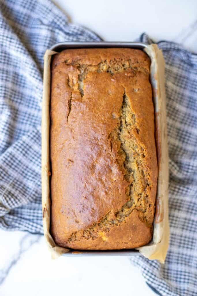 a fresh loaf of sourdough banana bread resting on a blue tea towel. 
